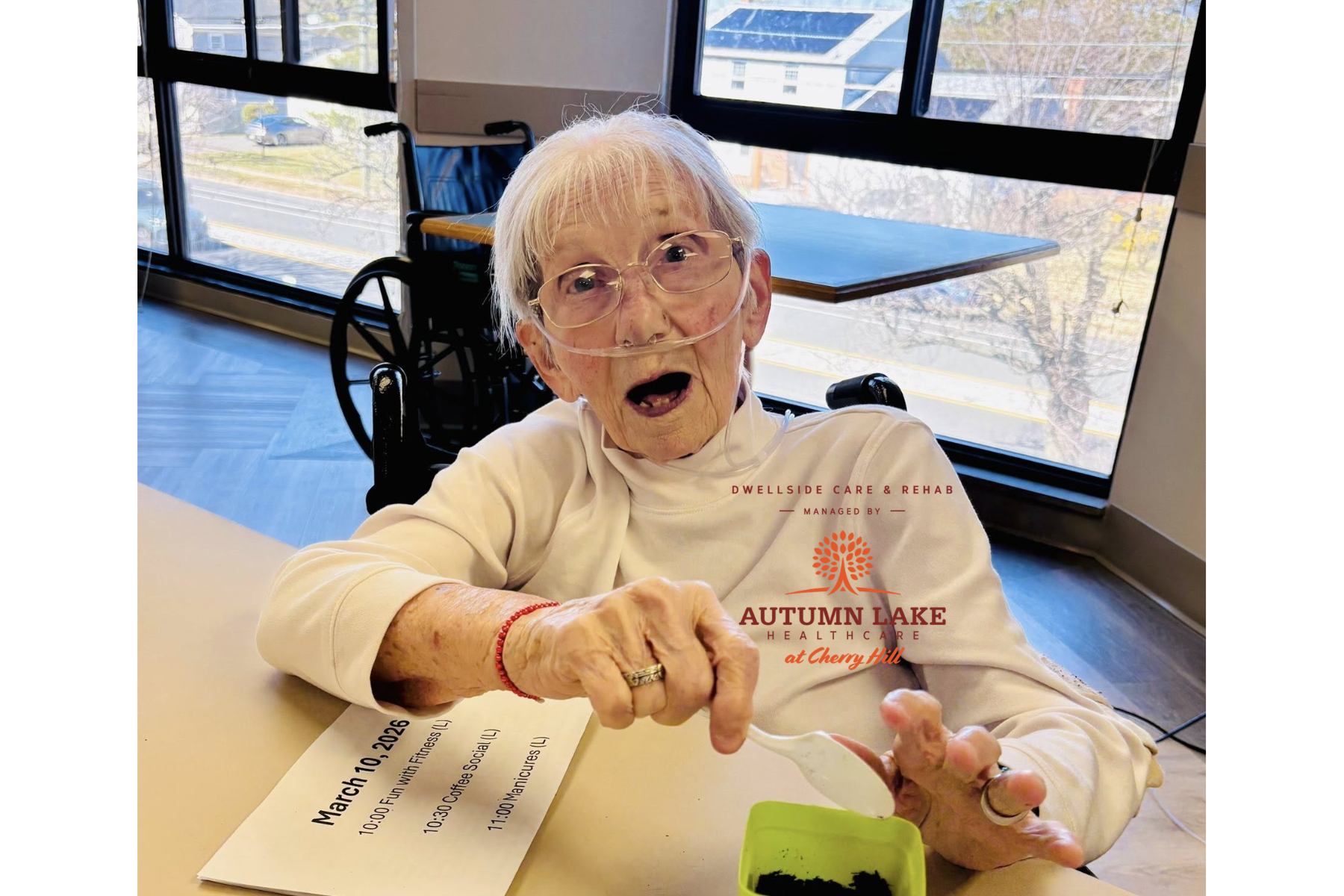 An elderly resident in a senior living community smiles while participating in a gardening activity, using a spoon to add soil to a small green pot.