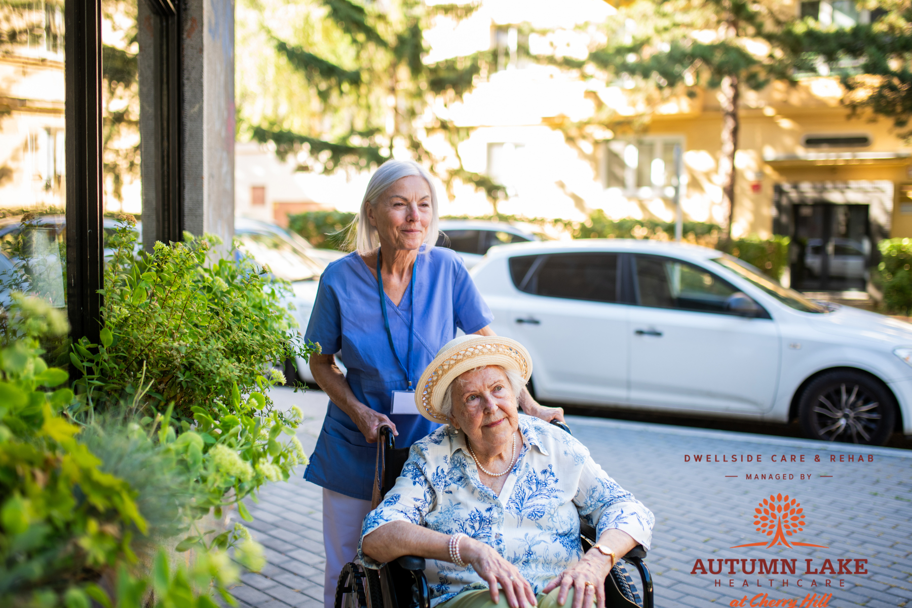 Nurse pushing a senior woman in a wheelchair outdoors at a nursing home.